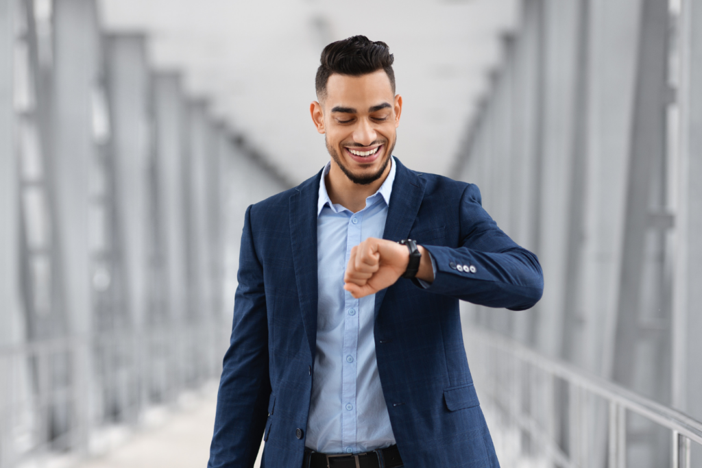 A man in a suit is smiling while looking at his wrist watch.